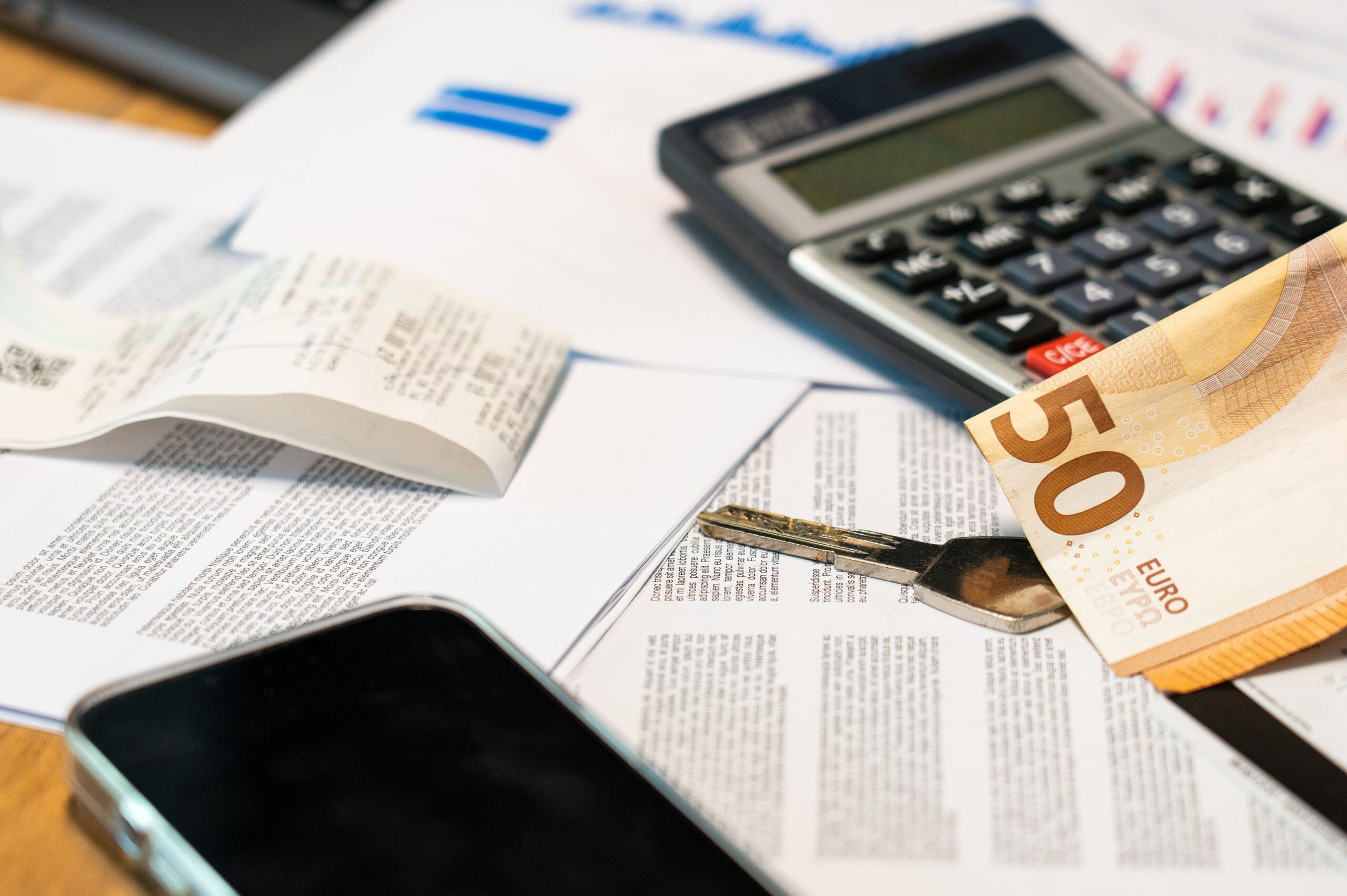Calculadora, boletos, documentos e cédula de dinheiro sobre a mesa, representando o cálculo de reajuste e custos do plano de saúde